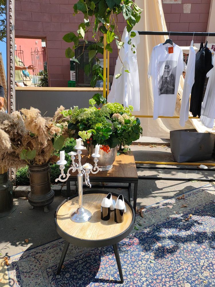 Étal en plein air avec un chandelier, des miroirs, des vêtements et un tapis ancien.