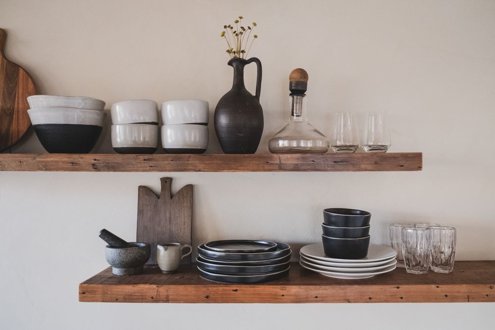 Bols, assiettes en céramique et verres disposés sur deux étagères de bois brut.