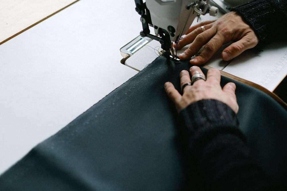 Mains guidant un tissu sombre sous l’aiguille d’une machine à coudre.