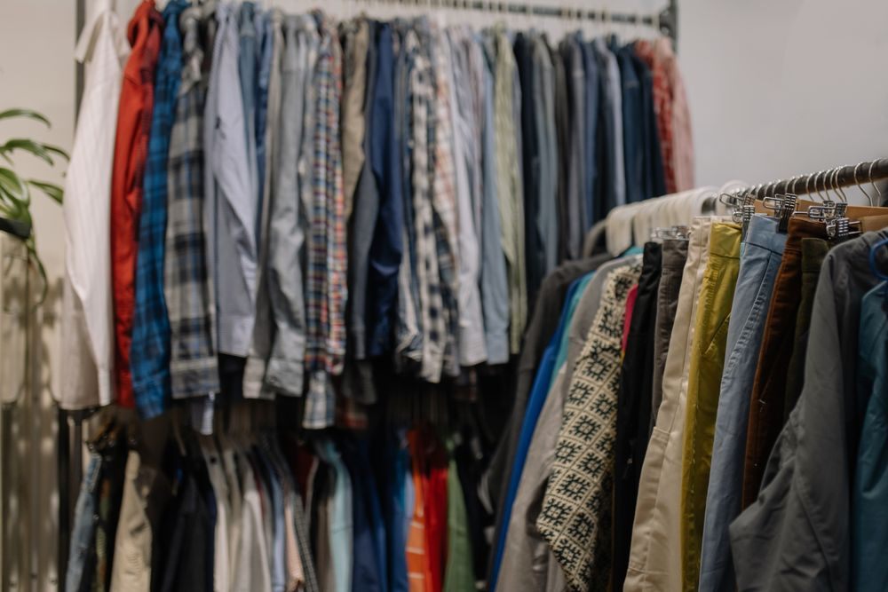 Deux portants de vêtements de seconde main, chemises et pantalons sur cintres.