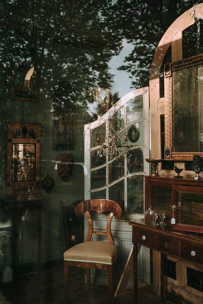 Vitrine d’antiquités présentant une chaise en bois, des miroirs anciens et un lustre.